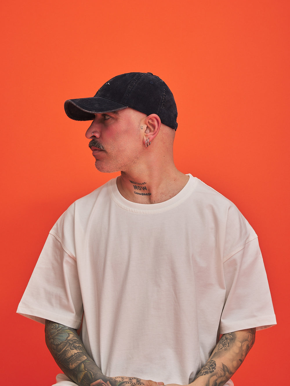 Man wearing a navy blue corduroy cap and white t-shirt against an orange background