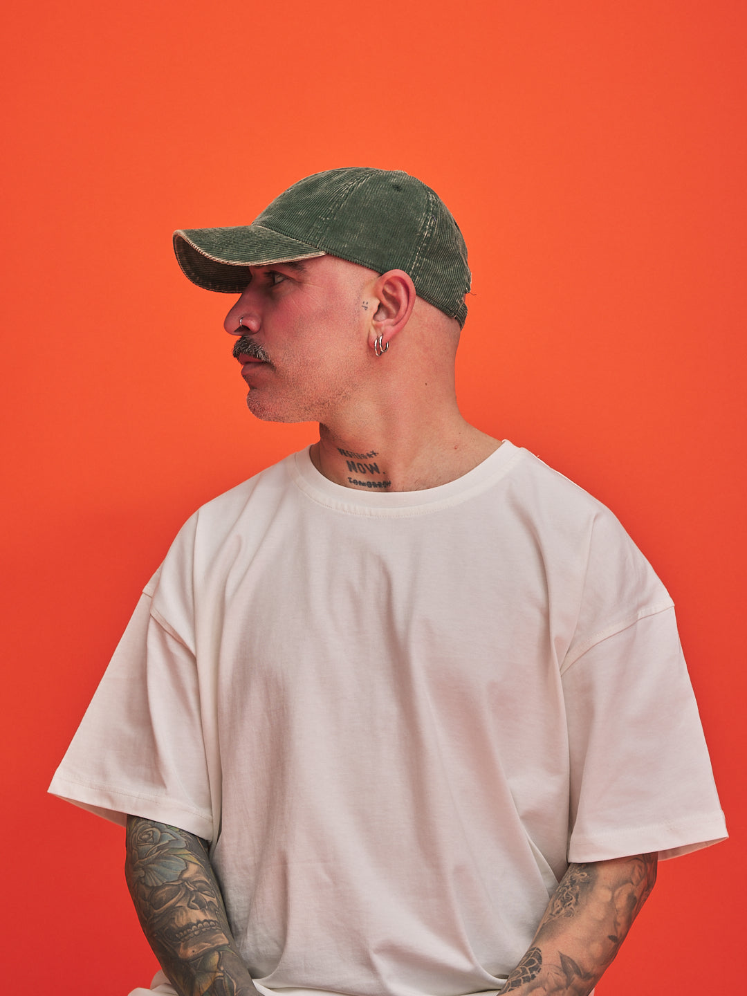 Man wearing a green cap and beige t-shirt against an orange background