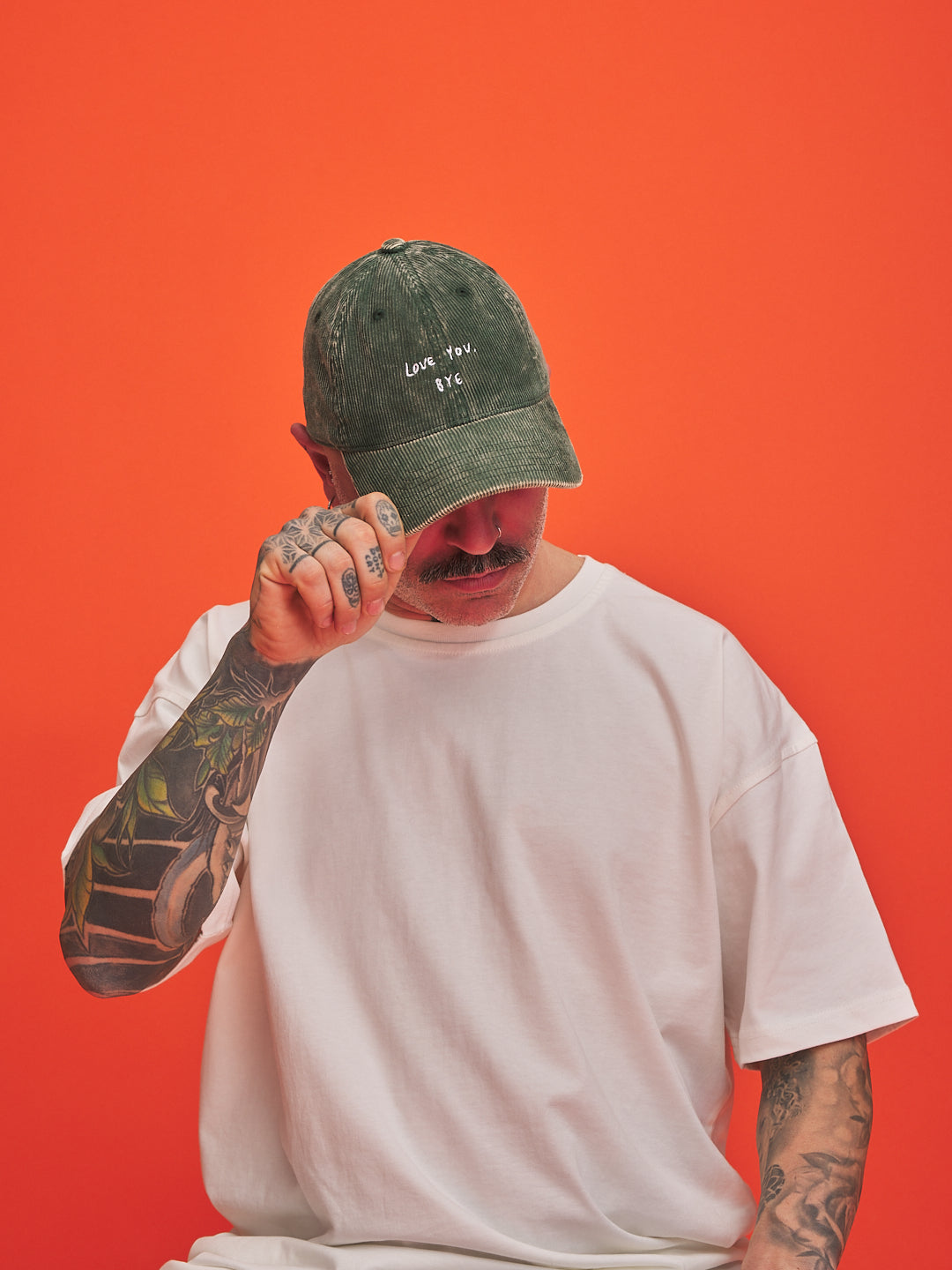 Person wearing a green cap and white t-shirt against an orange background