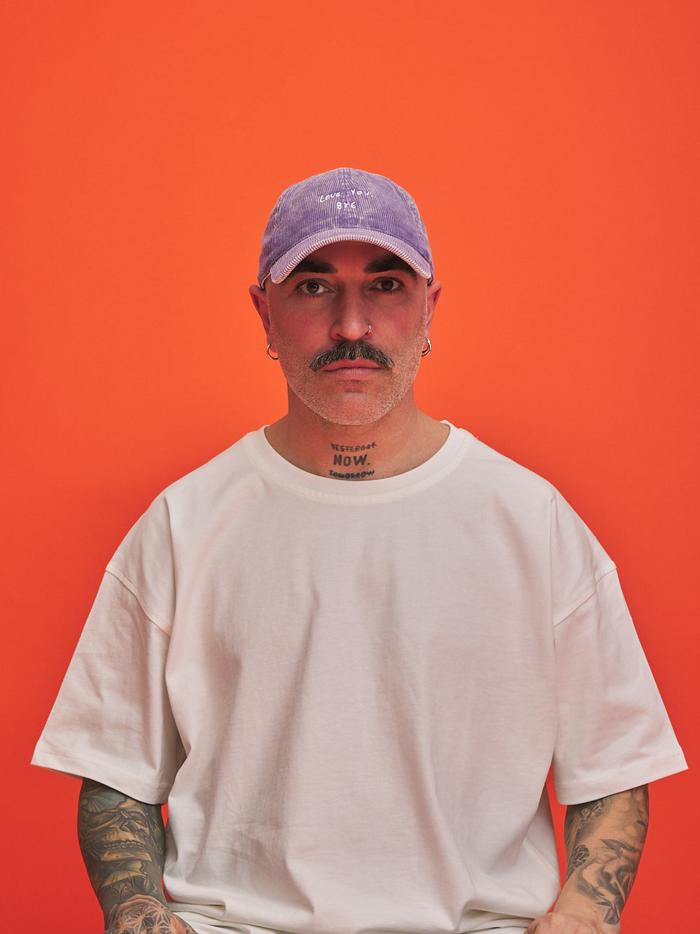 Man wearing a white t-shirt and purple cap against an orange background