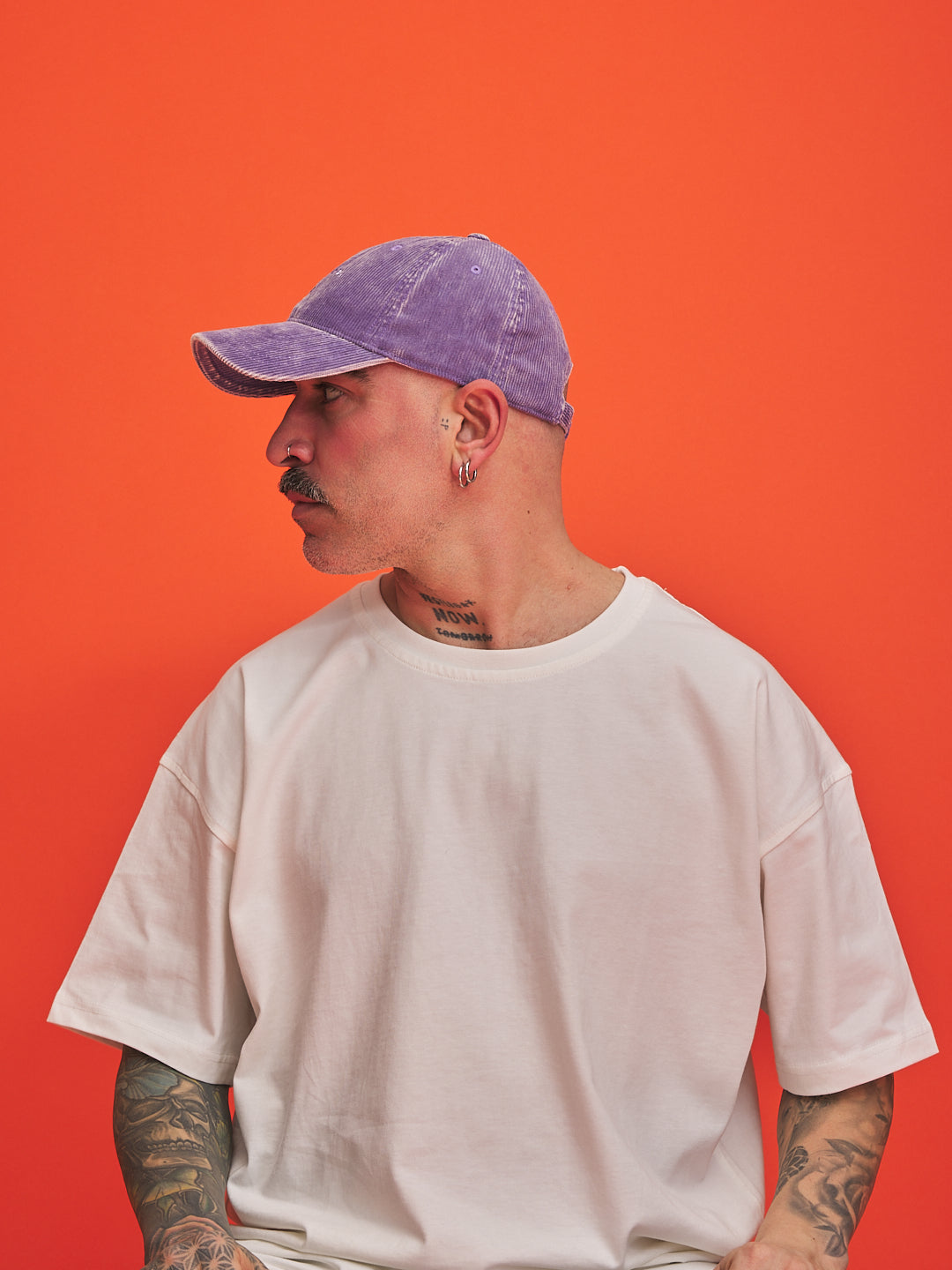 Person wearing a purple cap and white t-shirt against an orange background