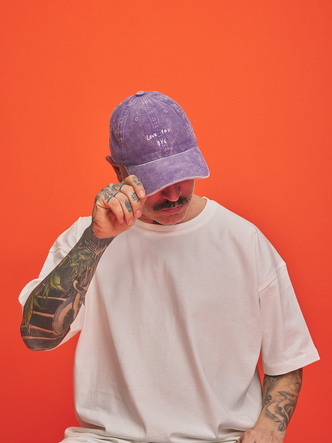 Person wearing a purple cap and white t-shirt against an orange background
