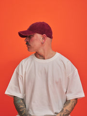Person wearing a red corduroy cap and white t-shirt against an orange background