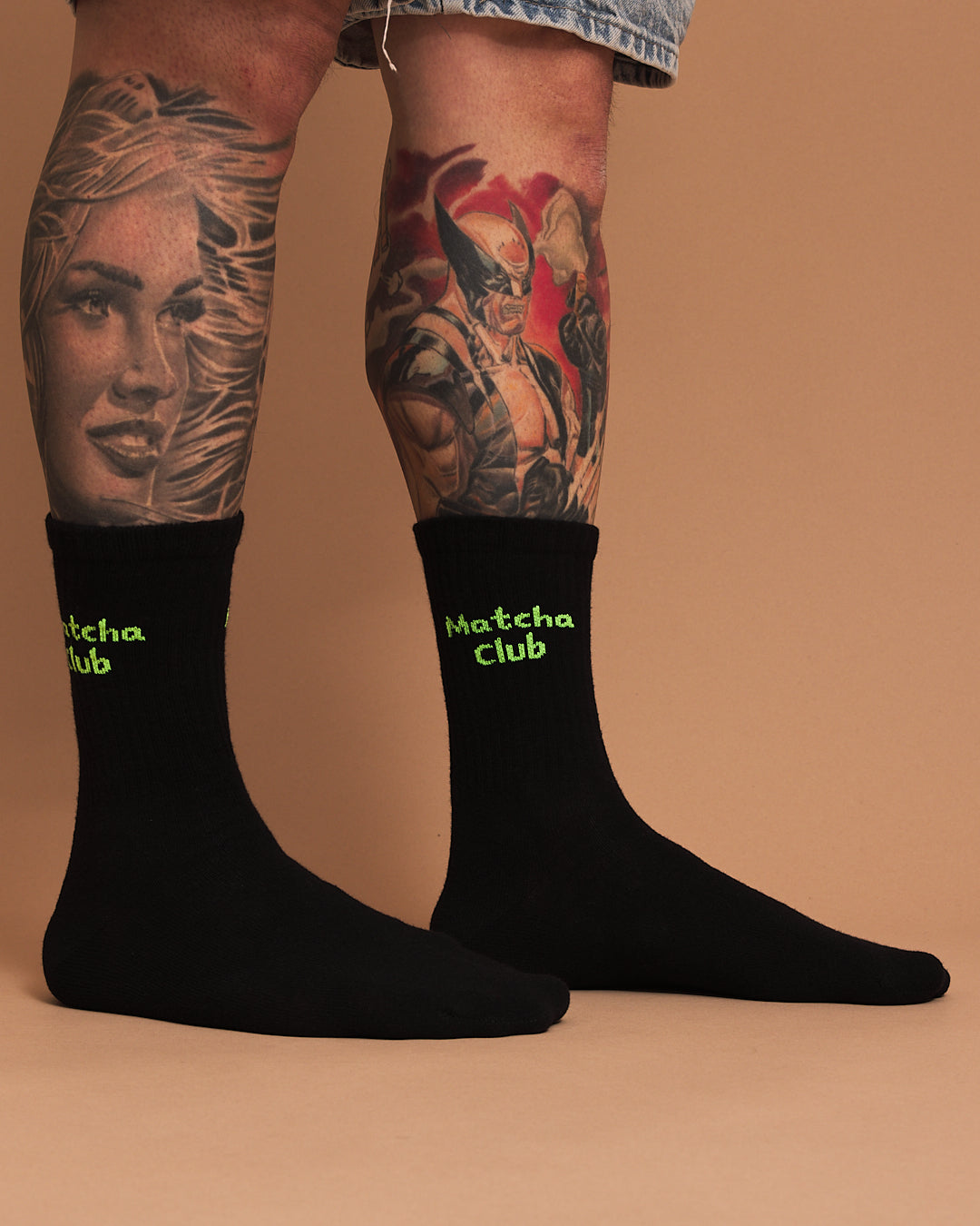 Black socks with 'Matcha Club' text worn by a person with tattoos on a beige background