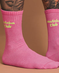Pink socks with 'Matcha Club' text worn by a person with tattoos on a brown background