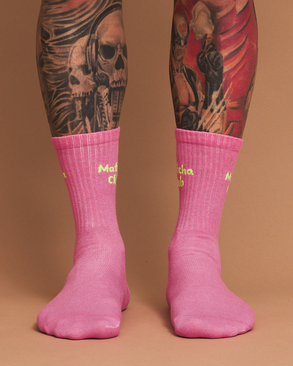 Pink socks with yellow text worn by a person with tattoos on a brown background