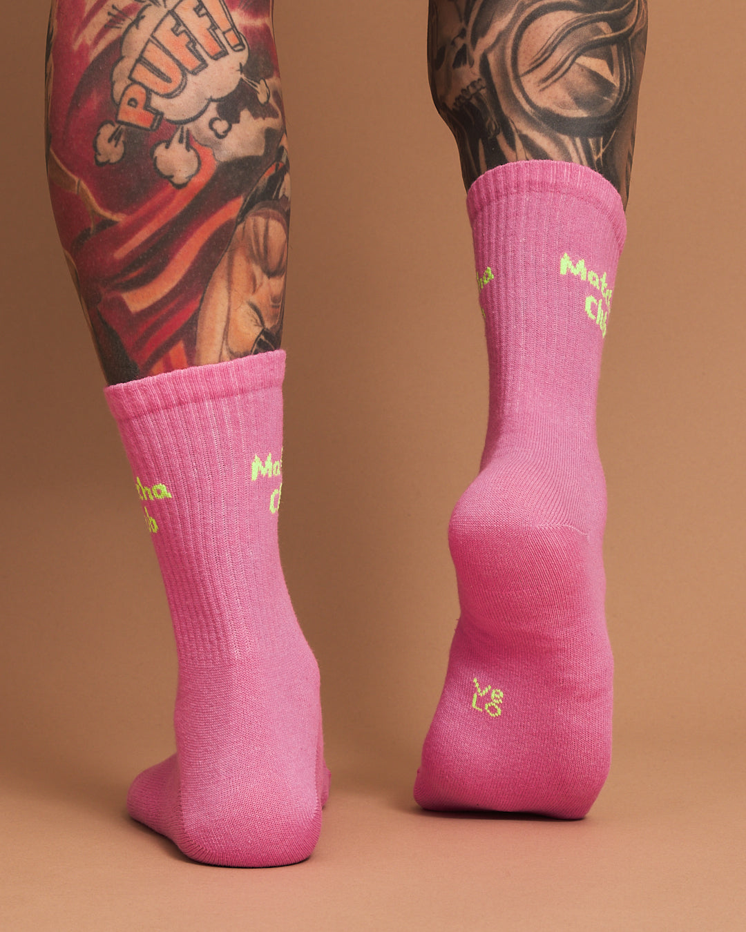 Pink socks with yellow text worn by a person with tattoos on a brown background