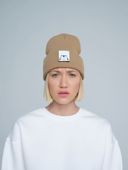 A person wearing mink brown colour beanie with cat illustration patch on the front