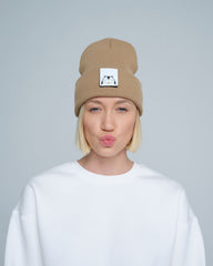 A person wearing mink brown colour beanie with cat illustration patch on the front on a gray background
