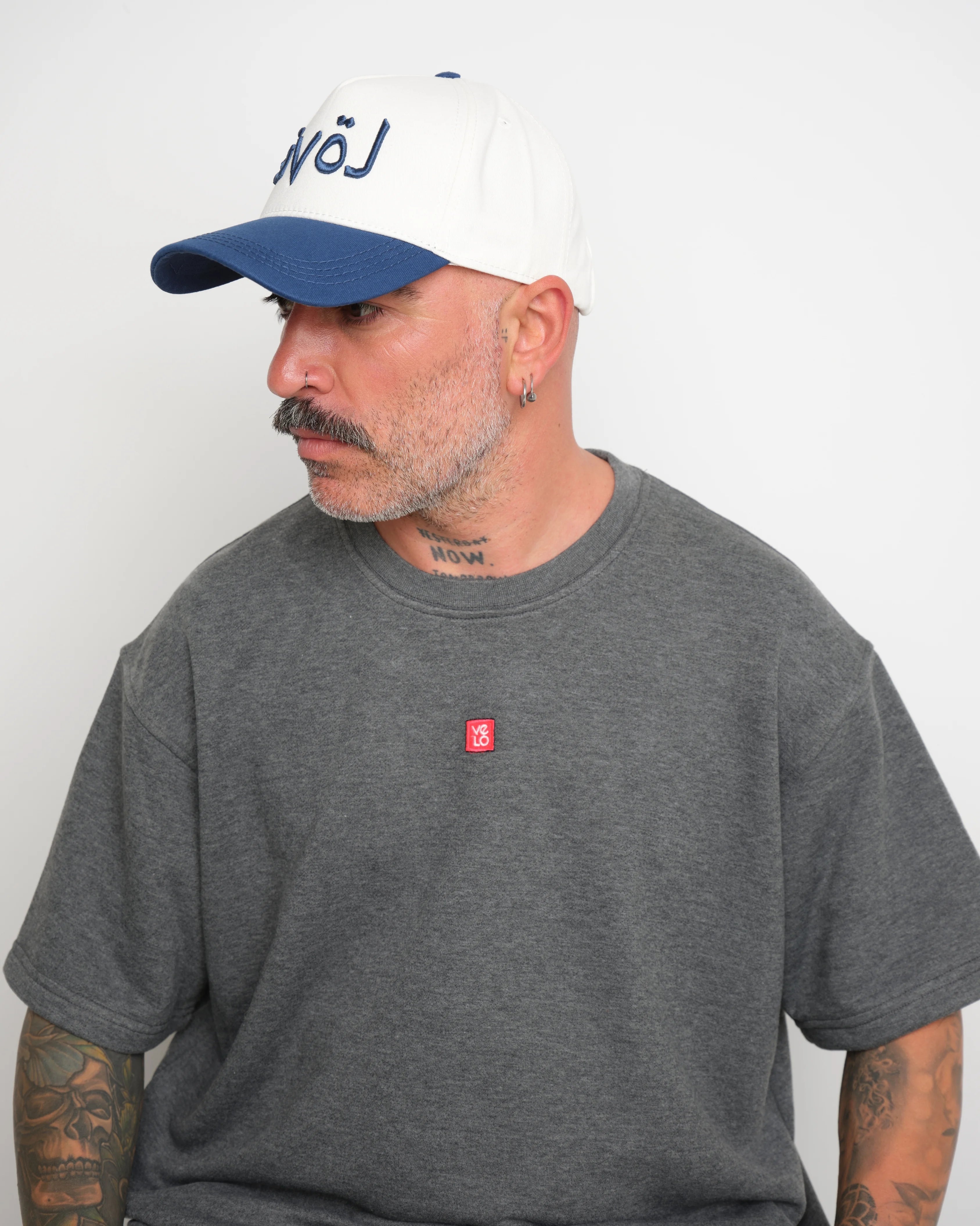 Man wearing a gray t-shirt with a small red logo and a white cap with navy brim and 'love' text.