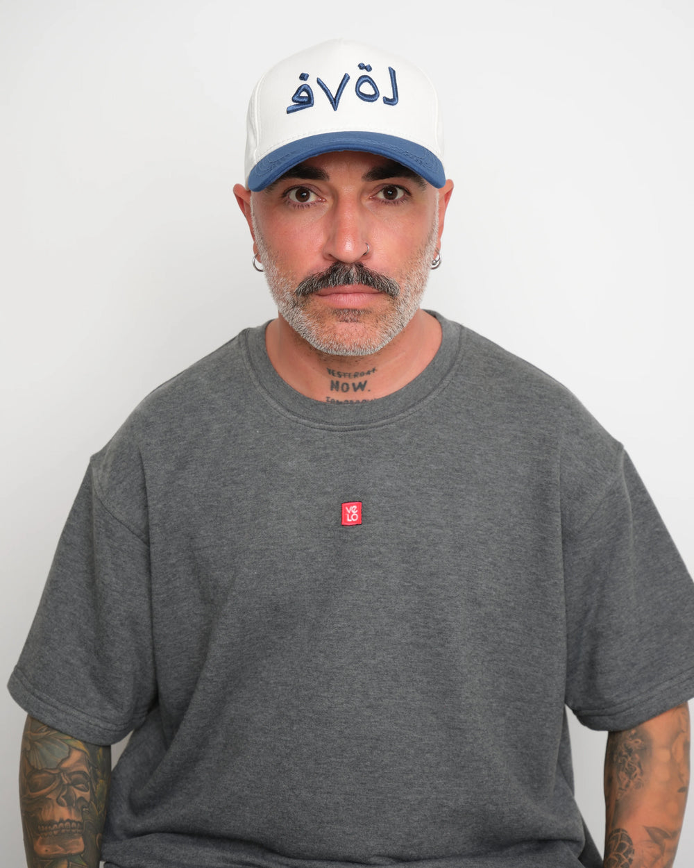 Man wearing a gray t-shirt with a small red logo and a white cap with navy brim and 'love' text.