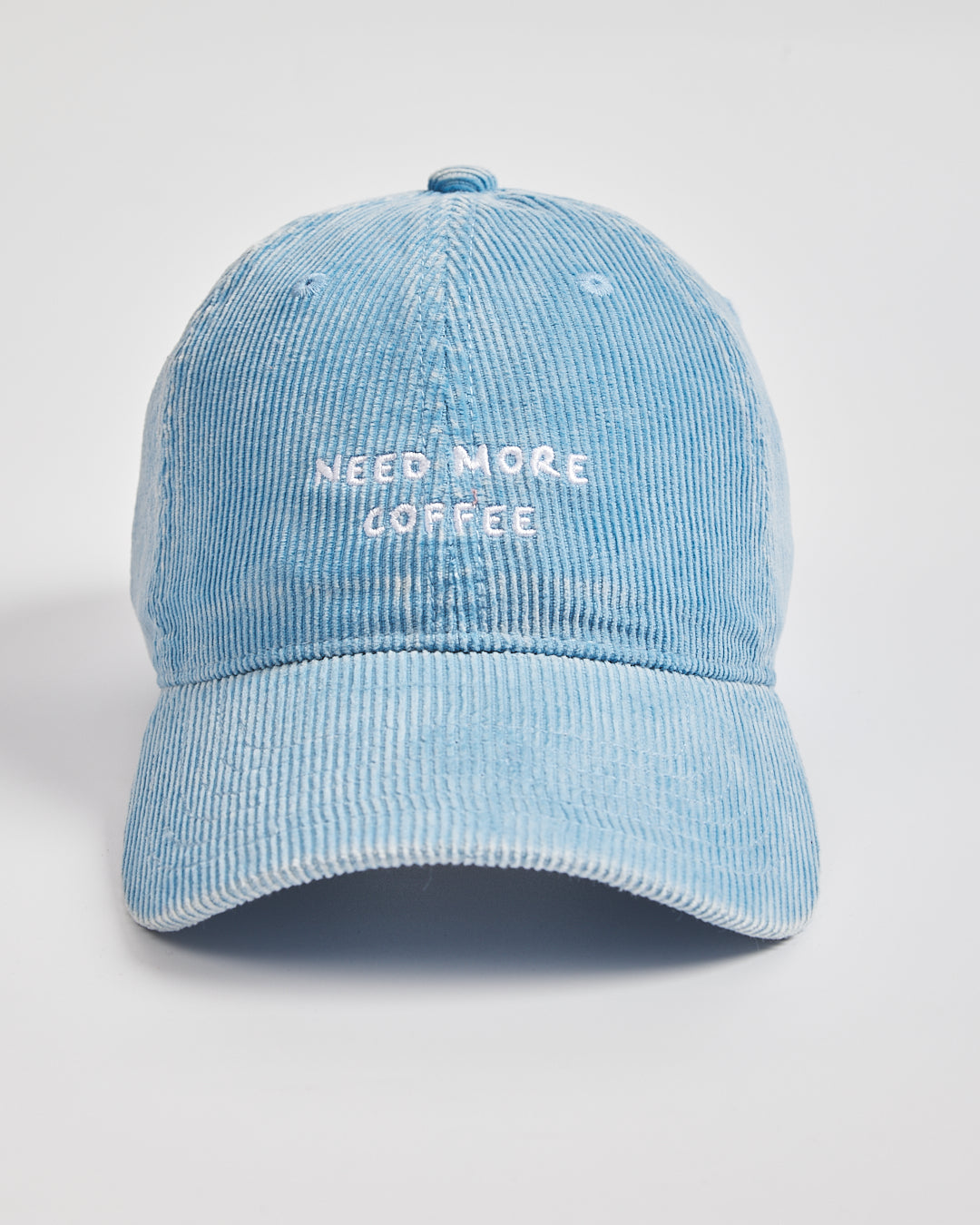 Light blue denim cap with 'Need More Coffee' text on a light gray background