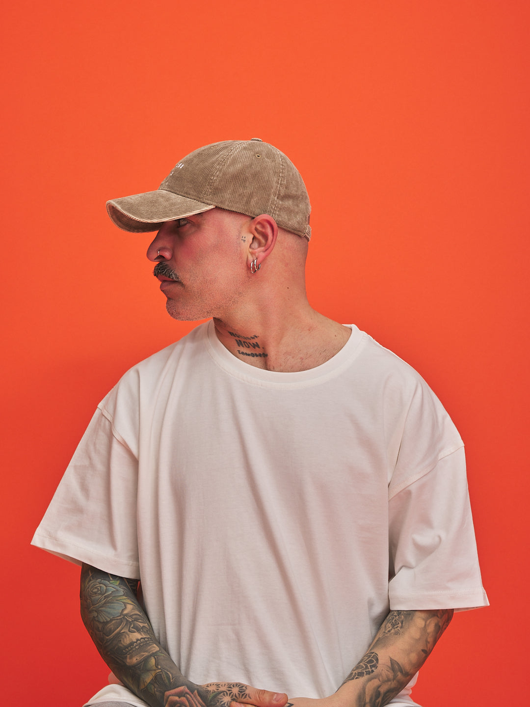 Person wearing a beige cap and white t-shirt against an orange background