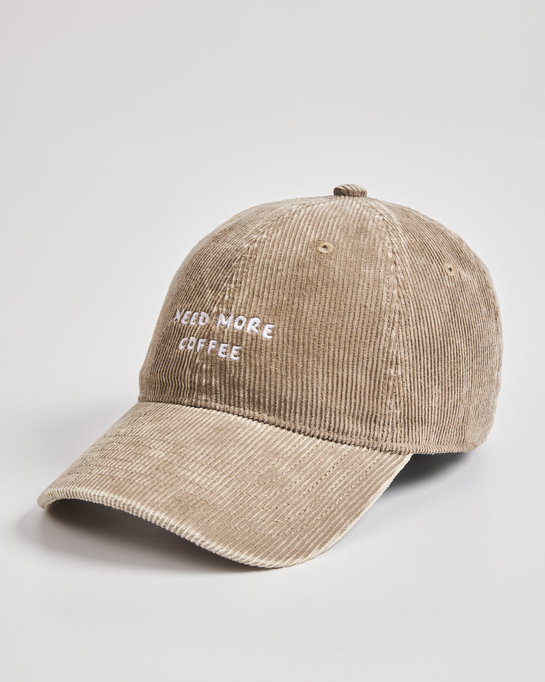 Beige corduroy cap with 'Need More Coffee' text on a light gray background