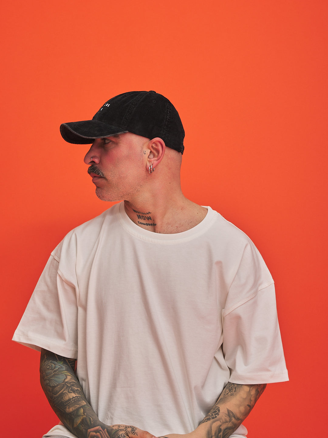 Person wearing a black cap and white t-shirt against an orange background