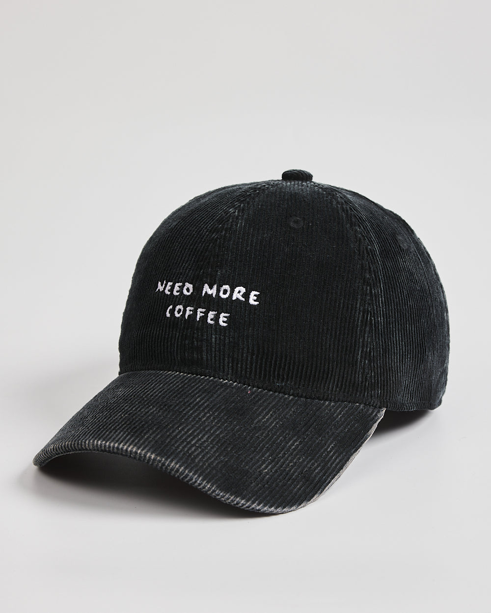 Black cap with 'NEED MORE COFFEE' text on a light gray background