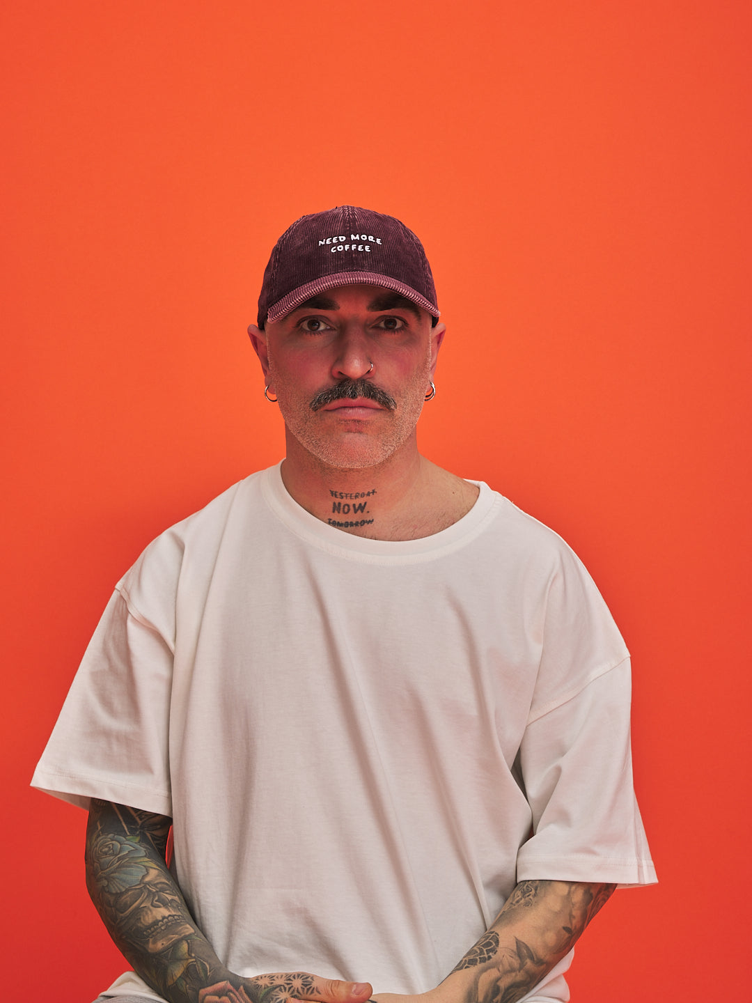 Man wearing a white t-shirt and dark cap against an orange background