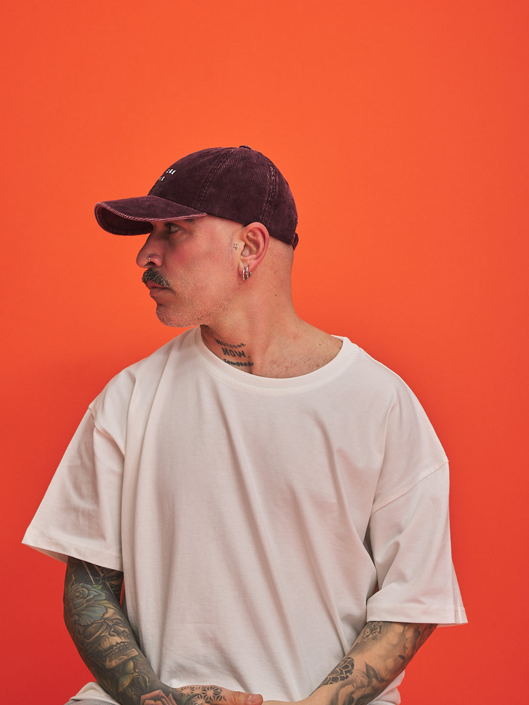 Man wearing a white t-shirt and dark cap against an orange background