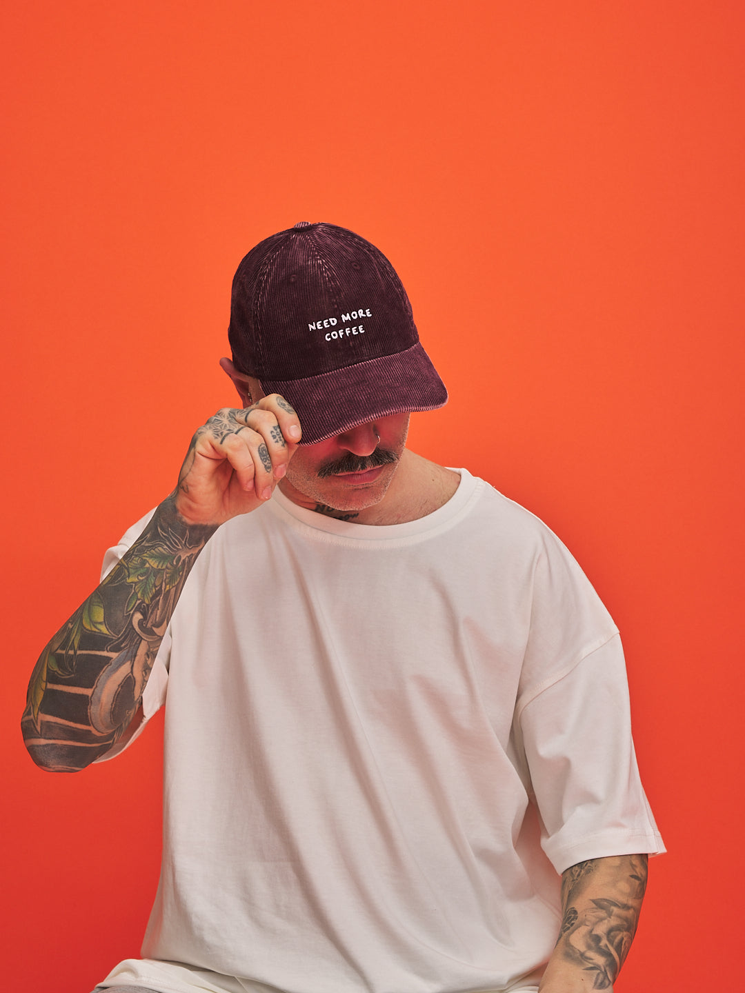 Person wearing a cap with 'Need More Coffee' text on an orange background