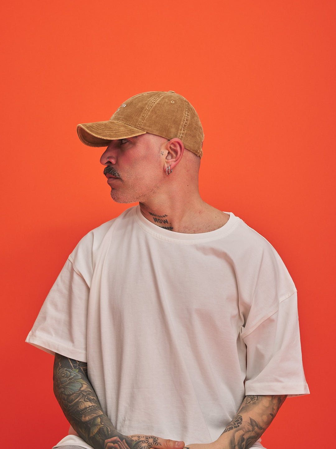 Man wearing a camel cap and white t-shirt against an orange background
