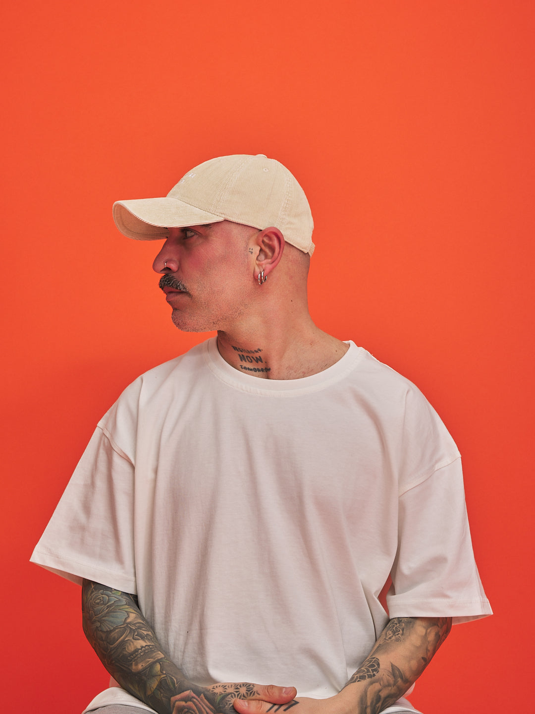 Man wearing a cream cap and white t-shirt against an orange background
