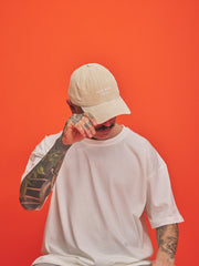 Person wearing a cream cap and white t-shirt against an orange background