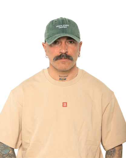 A man wearing the Need More Coffee Dark Green Washed Cap