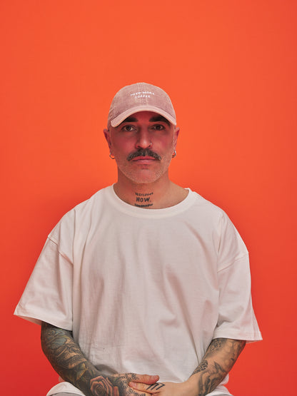 Man wearing a light pink cap and white t-shirt against an orange background