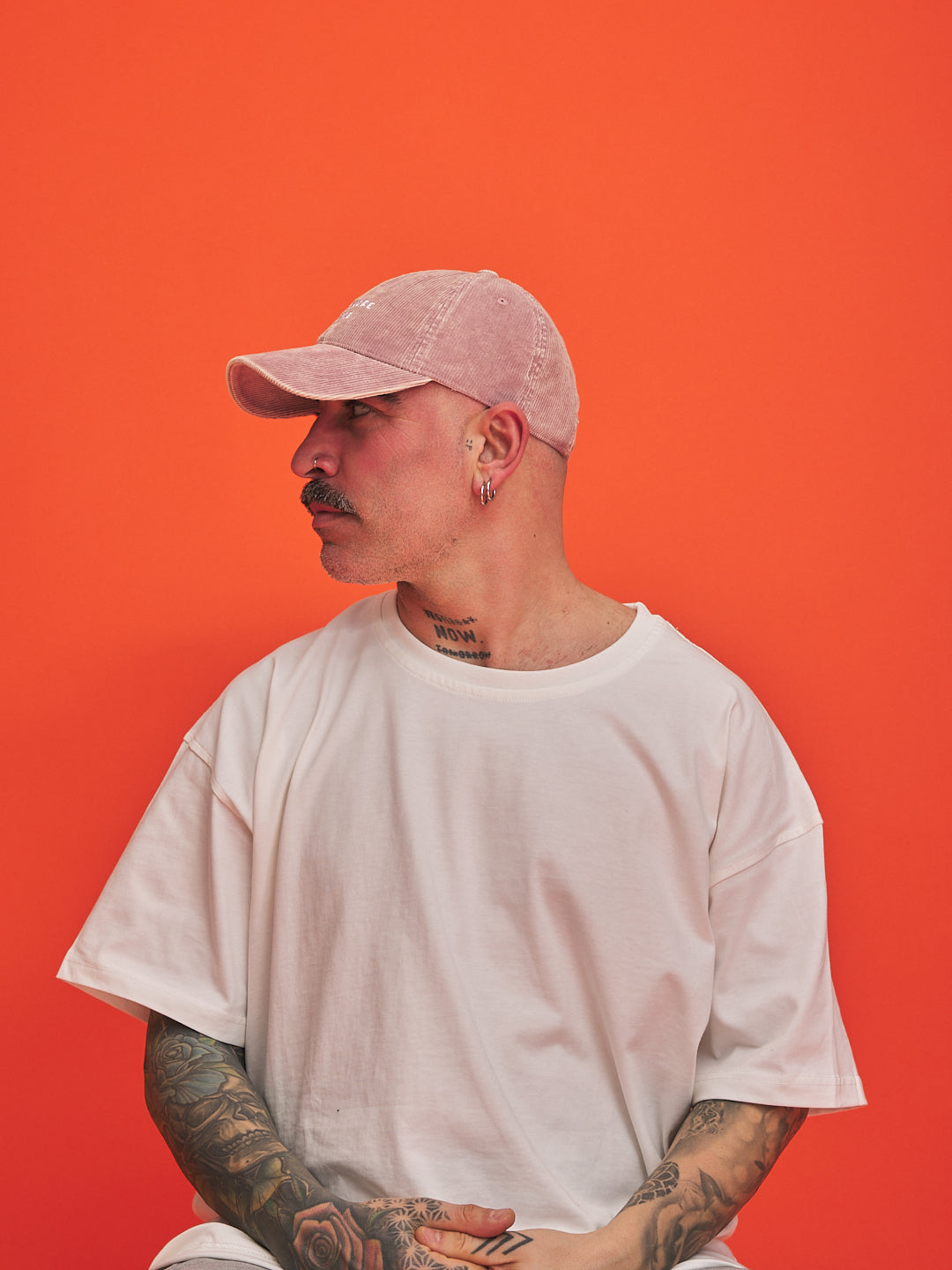 Person wearing a pink cap and white t-shirt against an orange background