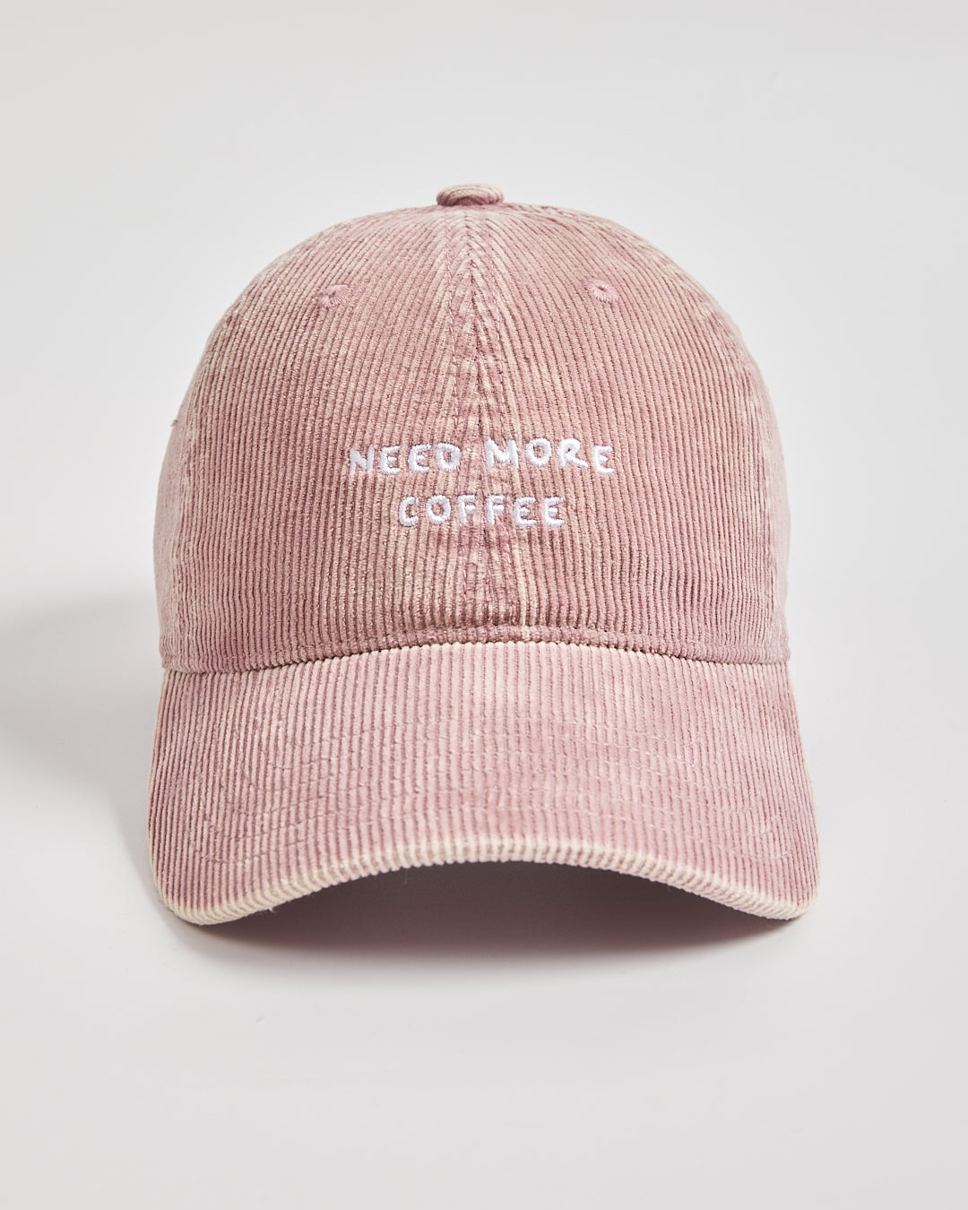 Pink corduroy cap with 'Need More Coffee' text on a light gray background