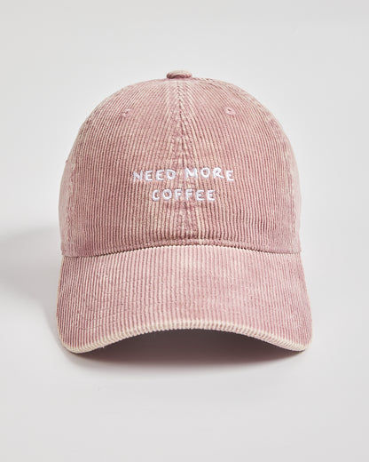 Pink corduroy cap with 'Need More Coffee' text on a light gray background