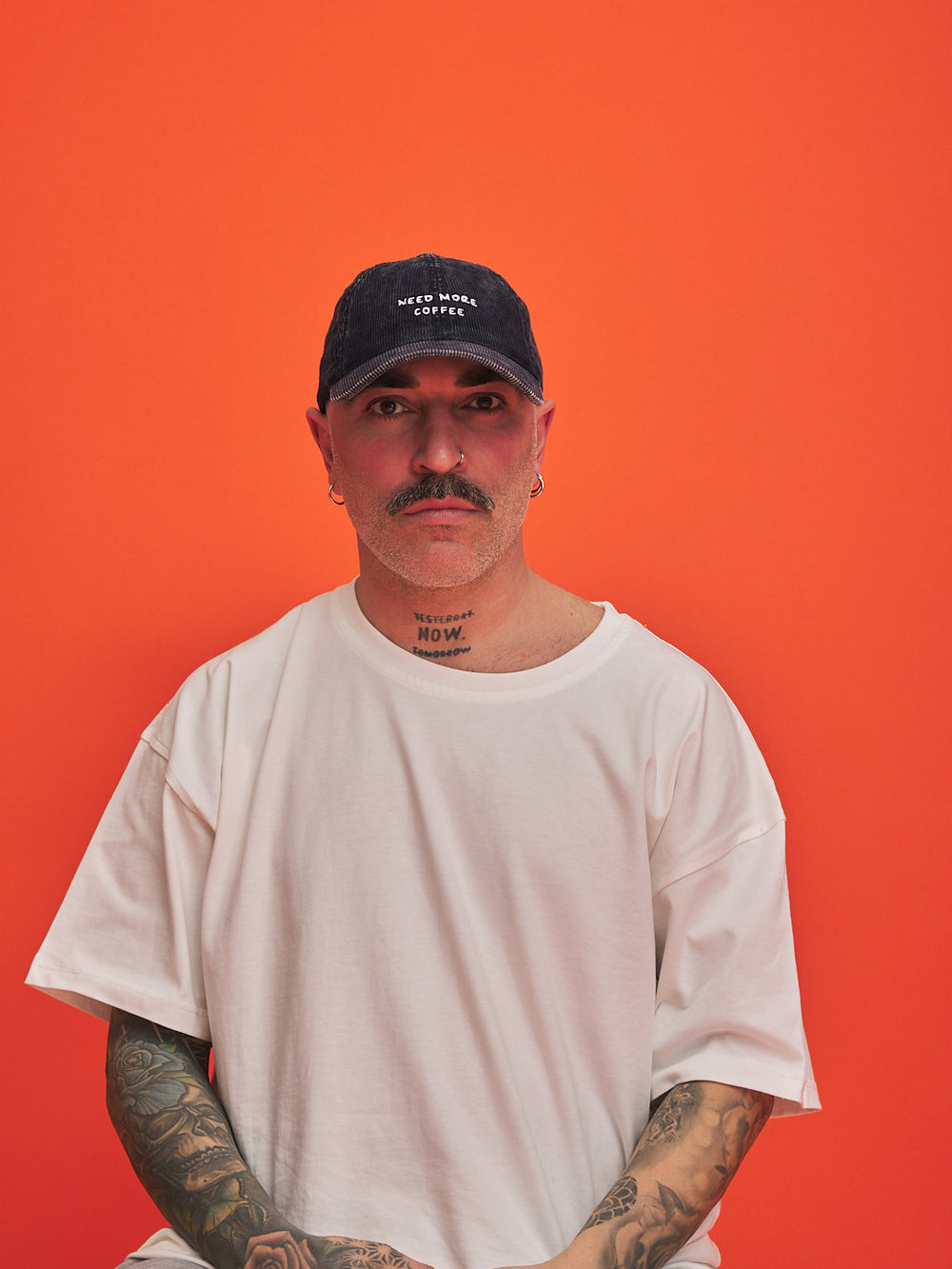 Man wearing a white t-shirt and navy cap against an orange background