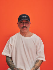 Man wearing a white t-shirt and navy cap against an orange background