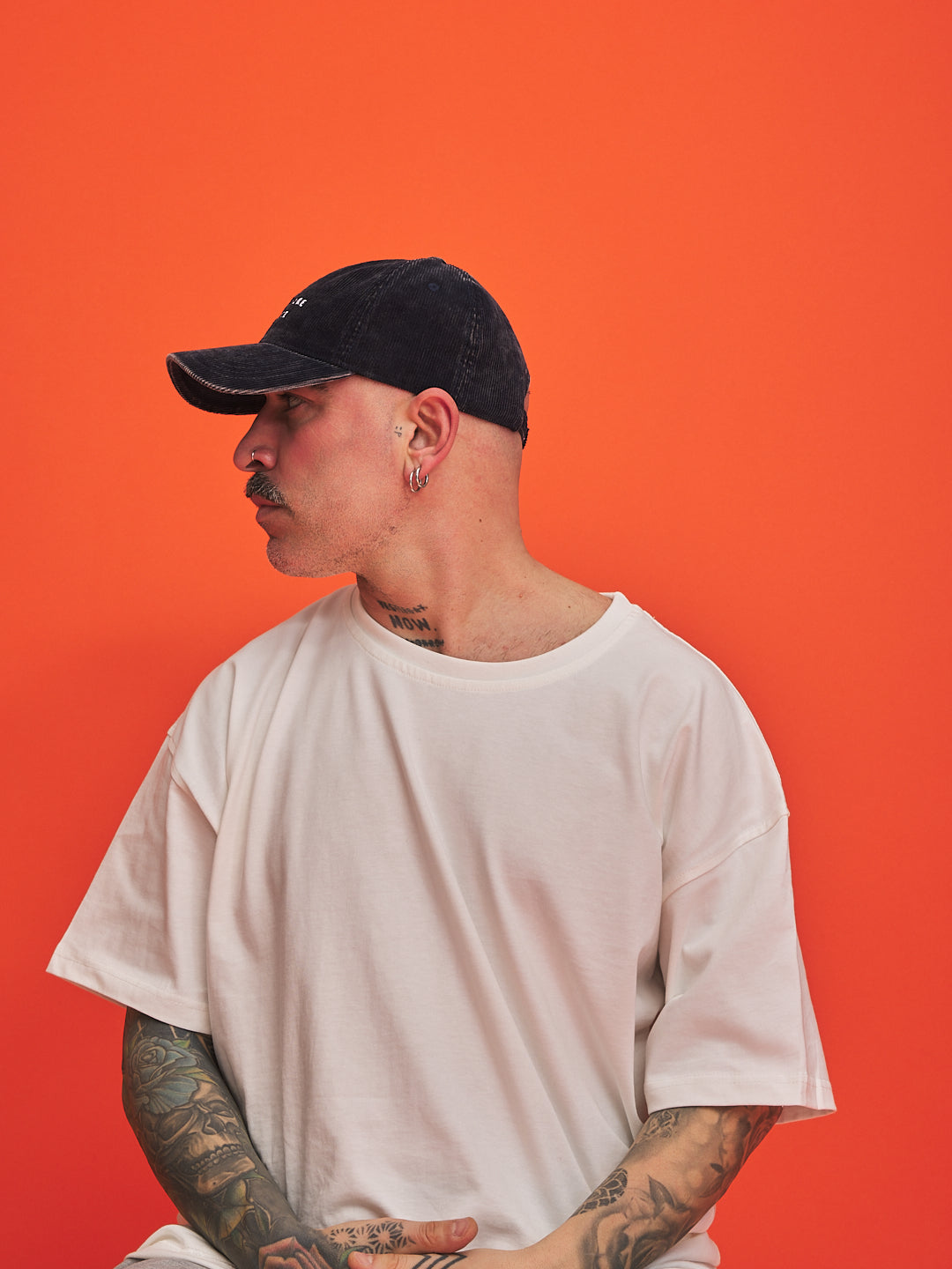 Person wearing a navy cap and white t-shirt against an orange background