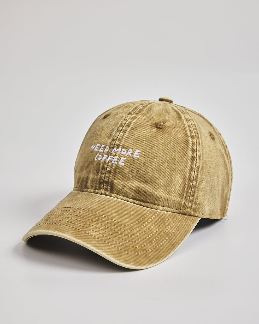 Beige cap with 'Need More Coffee' text on a light gray background