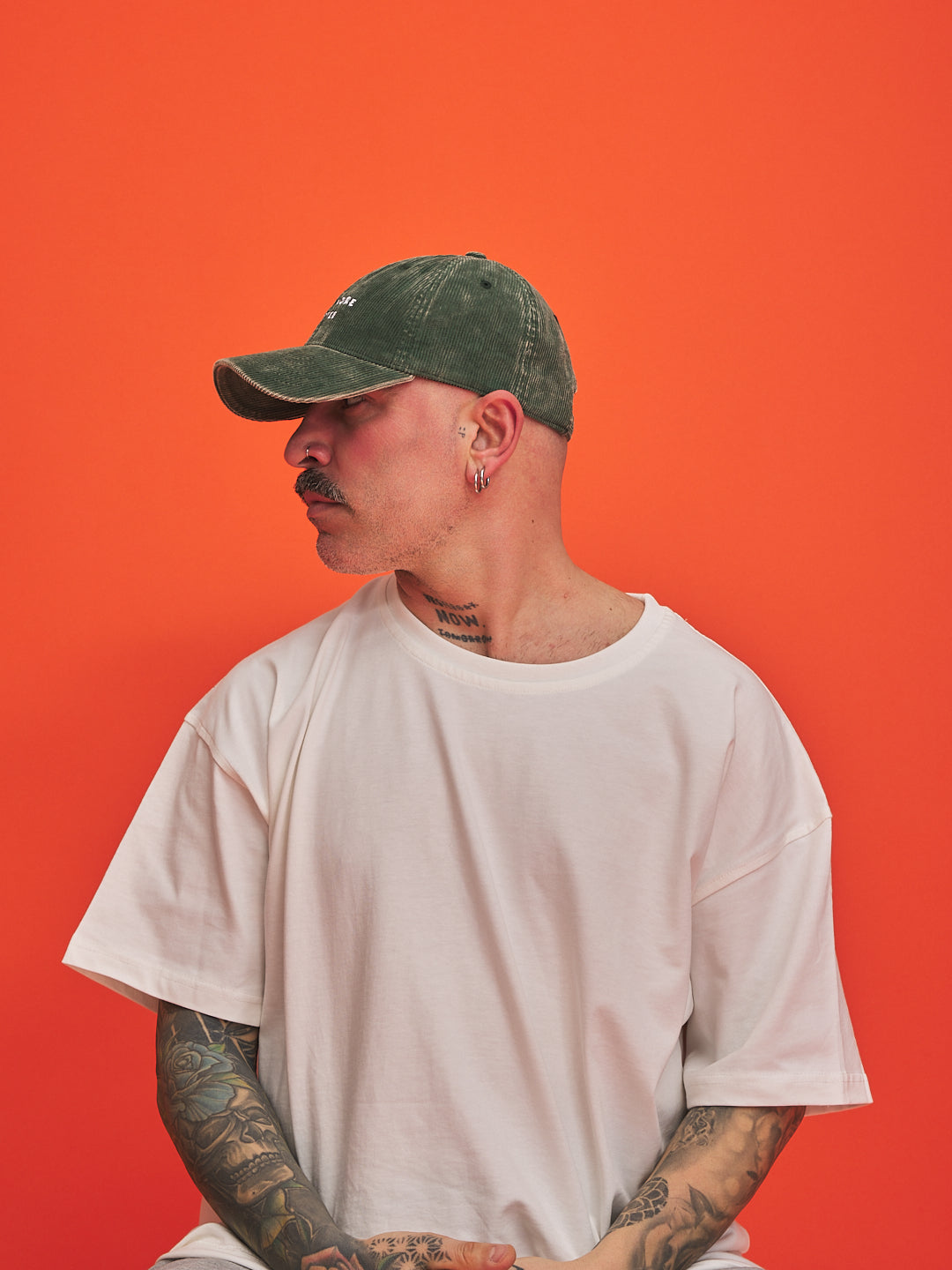 Person wearing a green cap and white t-shirt against an orange background