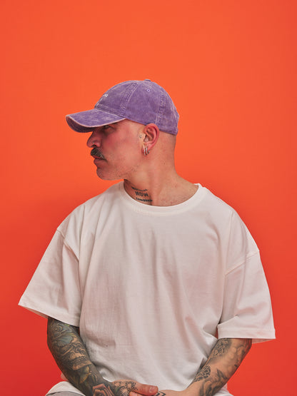 Person wearing a purple cap and white t-shirt against an orange background