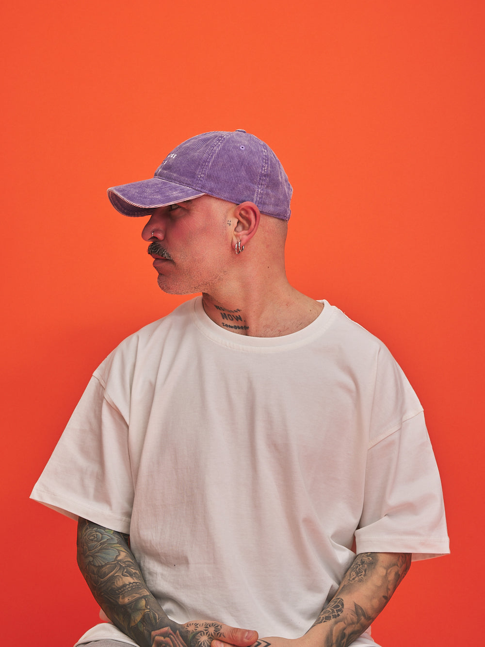 Person wearing a purple cap and white t-shirt against an orange background