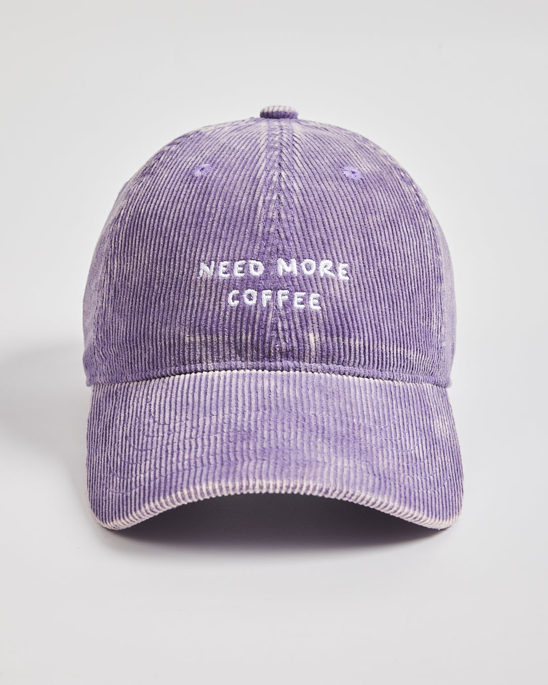 Purple corduroy cap with 'Need More Coffee' text on a light gray background