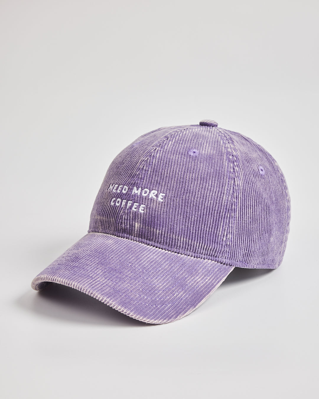 Purple cap with 'Need More Coffee' text on a light gray background
