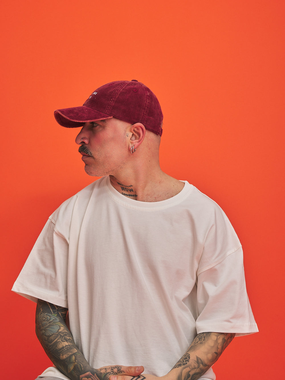 Person wearing a white t-shirt and maroon cap against an orange background