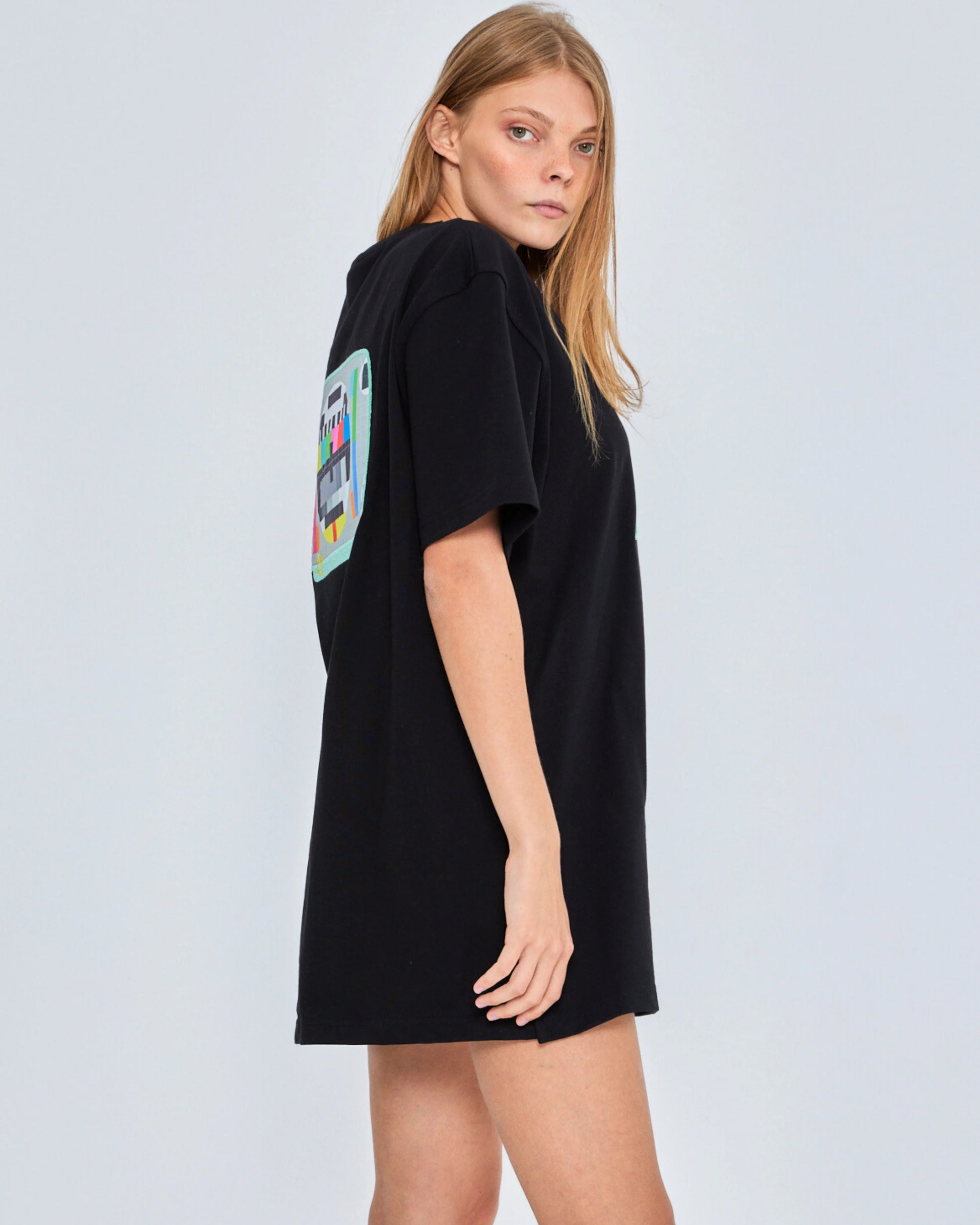 Woman wearing a black oversized t-shirt with a colorful graphic on the back against a light gray background