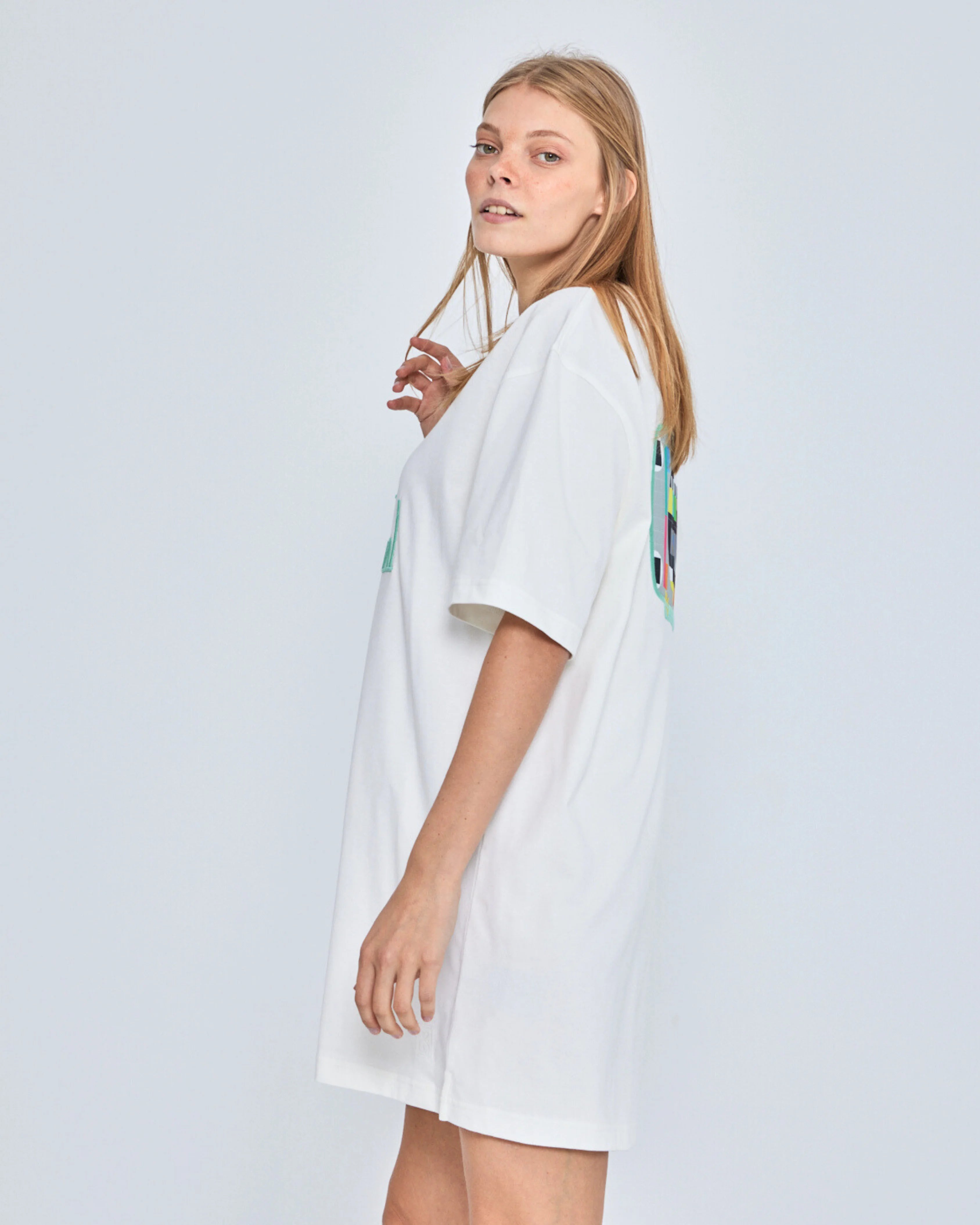 Woman wearing a white dress with colorful patterns on a plain background