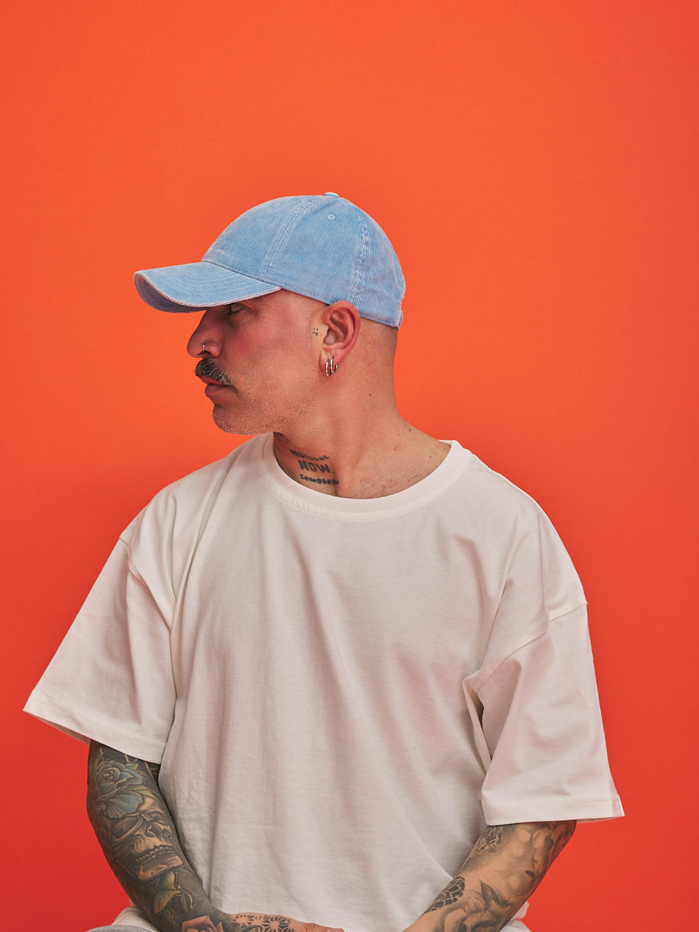 Person wearing a light blue cap and beige t-shirt against an orange background