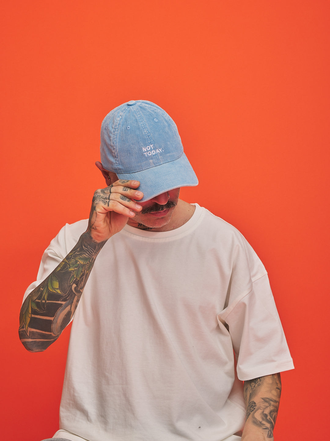 Person wearing a blue cap with text, covering their face against an orange background