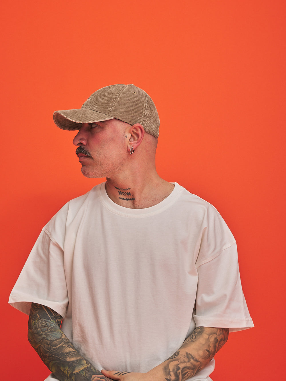 Man wearing a beige cap and white t-shirt against an orange background
