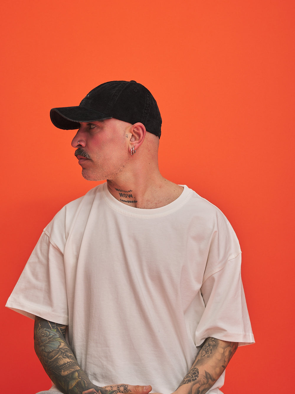 Person wearing a black cap and white t-shirt against an orange background