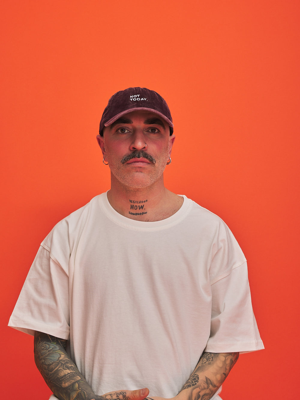 Man wearing a white t-shirt and dark cap against an orange background