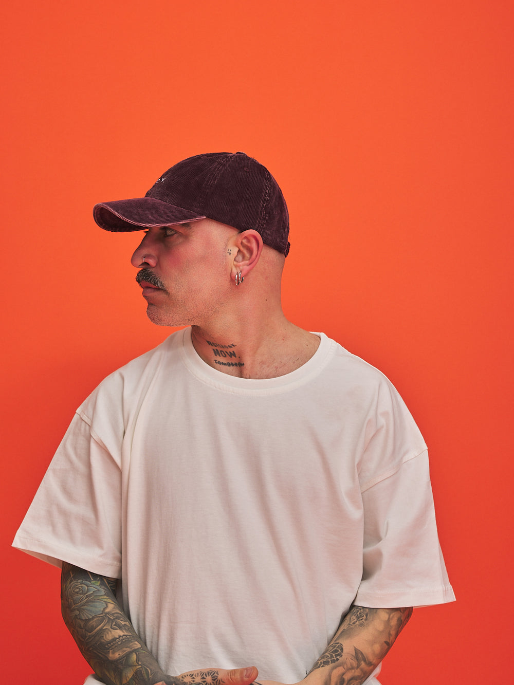 Person wearing a white t-shirt and dark cap against an orange background