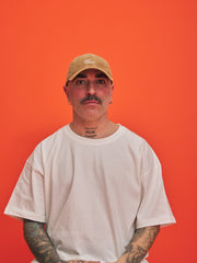 Man wearing a camel cap and white t-shirt against an orange background